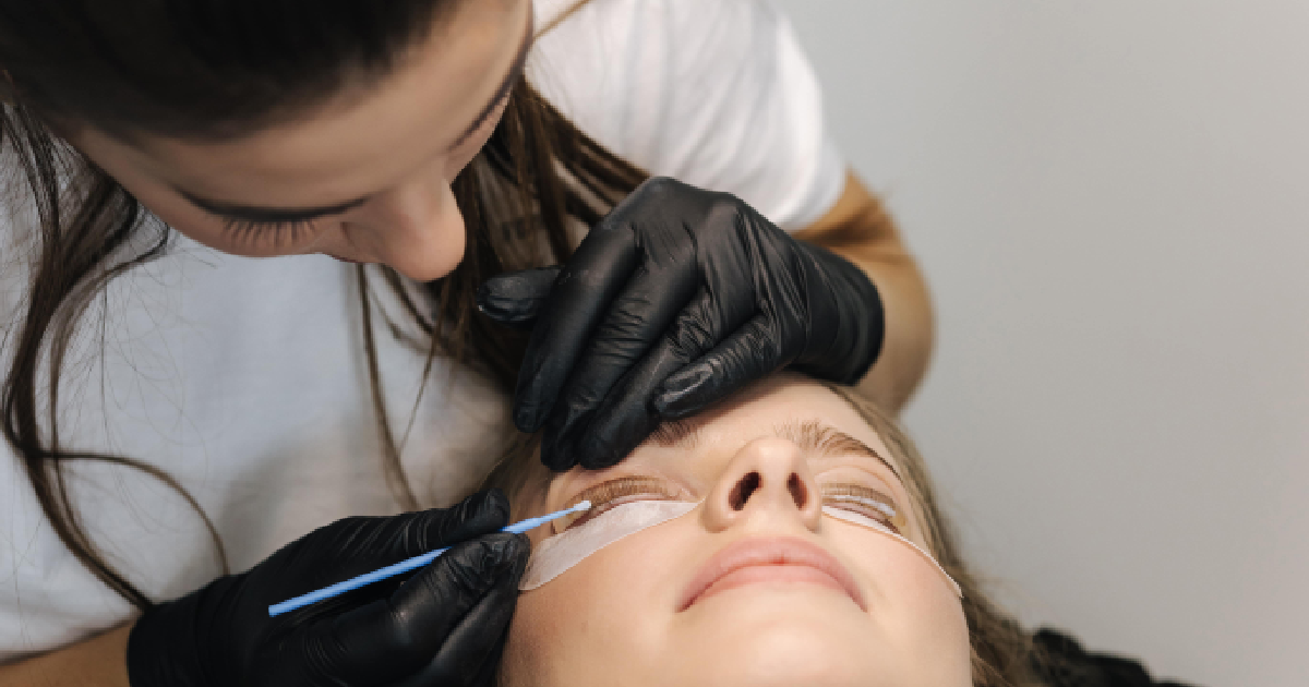 Beautician applies lash extensions to a woman lying down with eye pads in Albany, OR