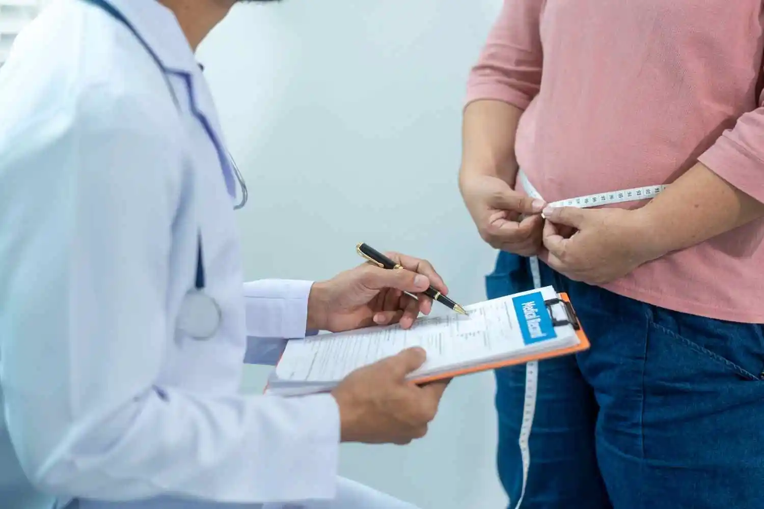 Healthcare provider discussing a personalized weight loss plan with a patient using a measuring tape and medical forms